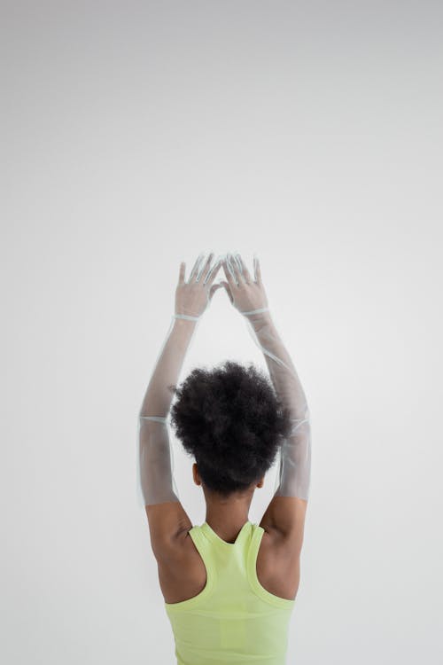 Back view of anonymous African American female in colorful outfit and blue gloves with arms raised on white background