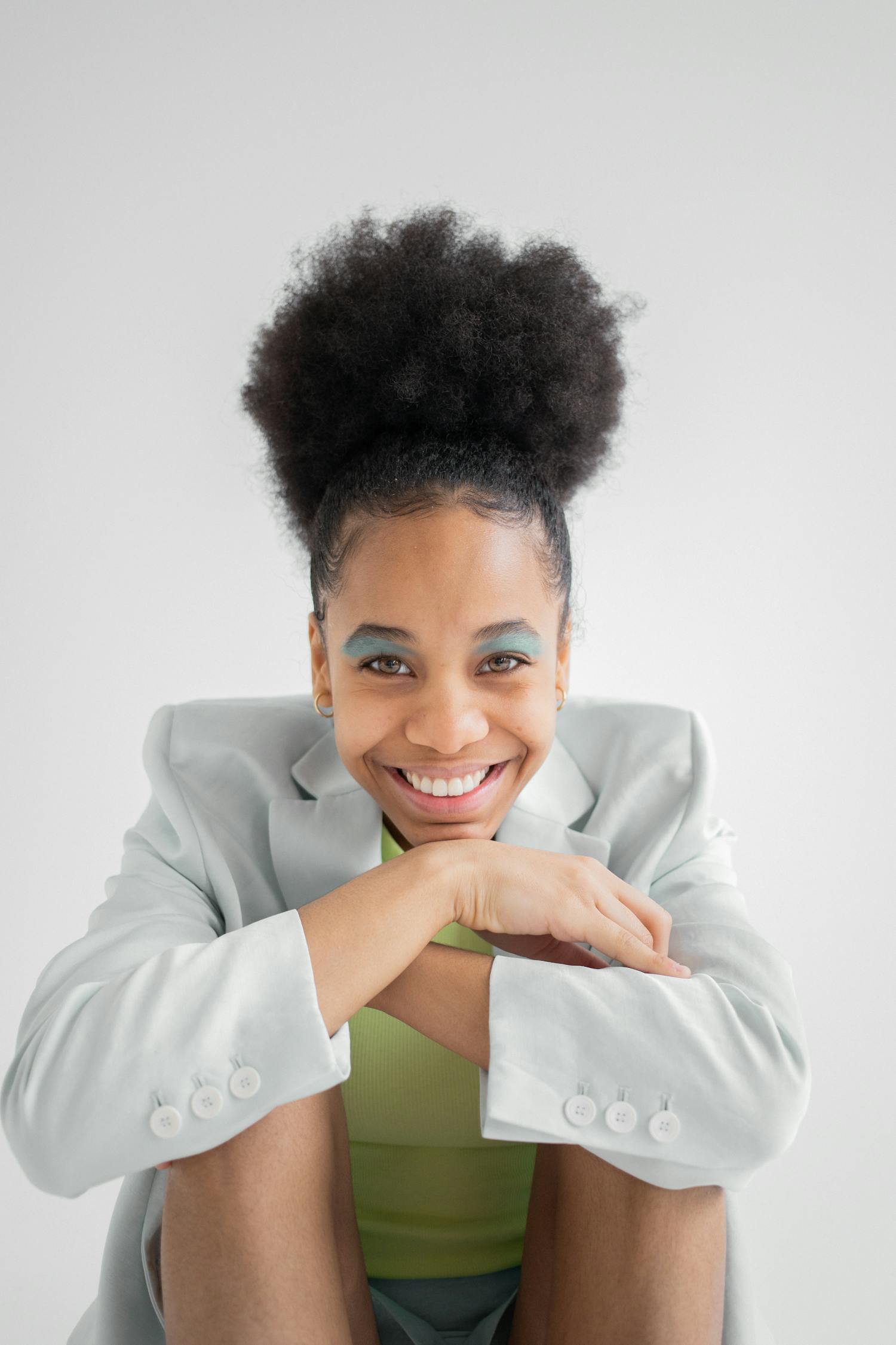 Smiling African American female model with curly hair and trendy visage sitting with bent legs and crossed arms