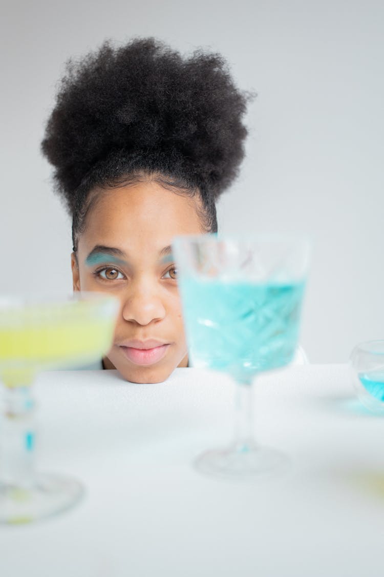 Black Woman Looking At Glasses With Colorful Liquid