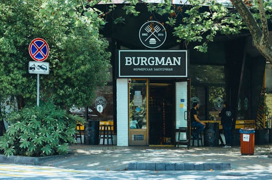 Exterior view of Burgman restaurant with outdoor seating area in a leafy urban setting.