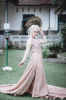 Asian bride poses outdoors in traditional attire and ornate headdress, capturing elegance and cultural beauty.