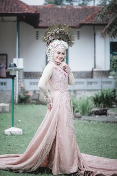 Beautiful woman posing in an elegant traditional wedding dress with a floral headdress outdoors.