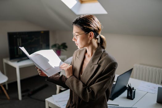 Professional woman in glasses reviewing financial documents at her office desk.