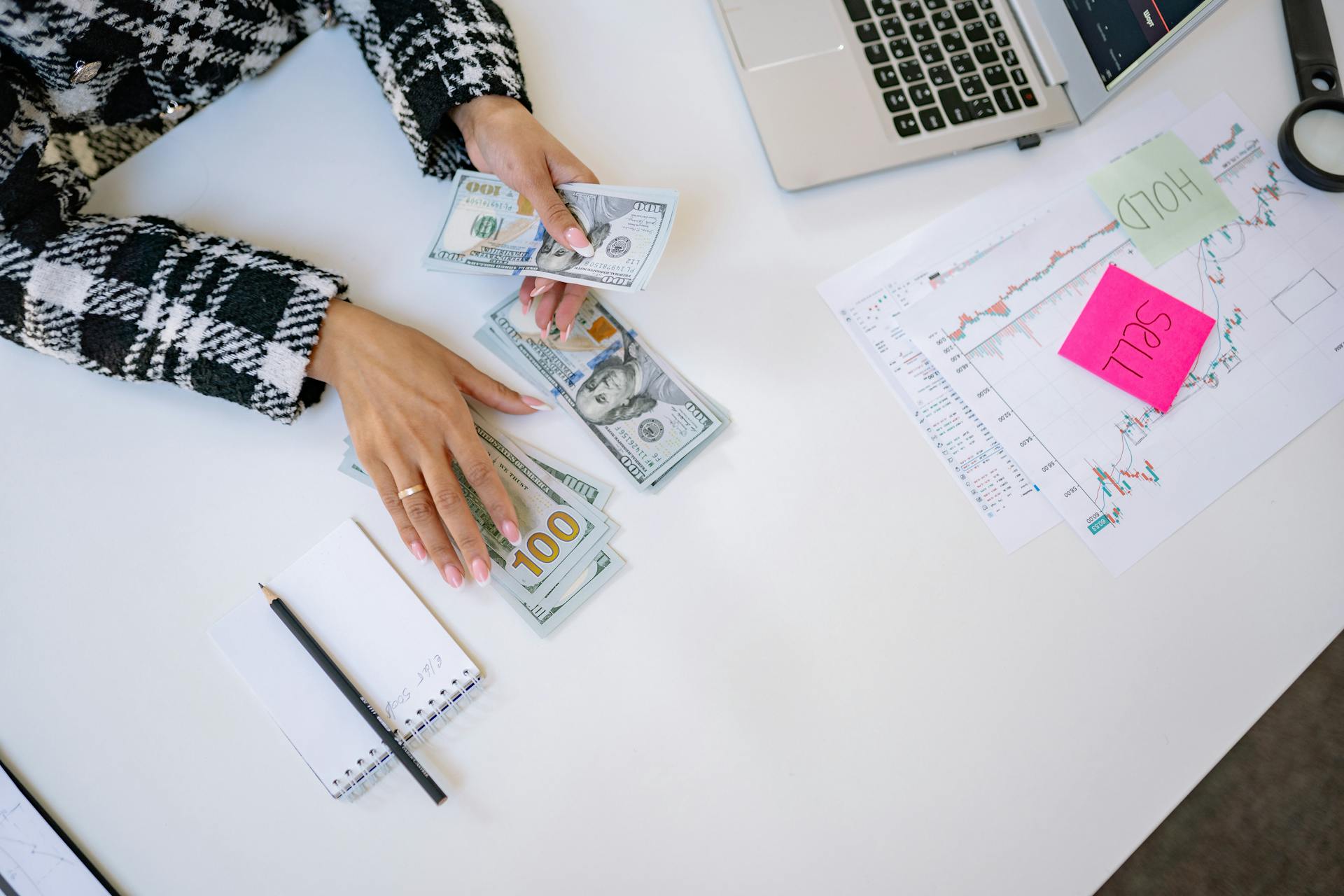 Businesswoman counting dollar bills with financial charts and laptop on table. Investment and finance concept.