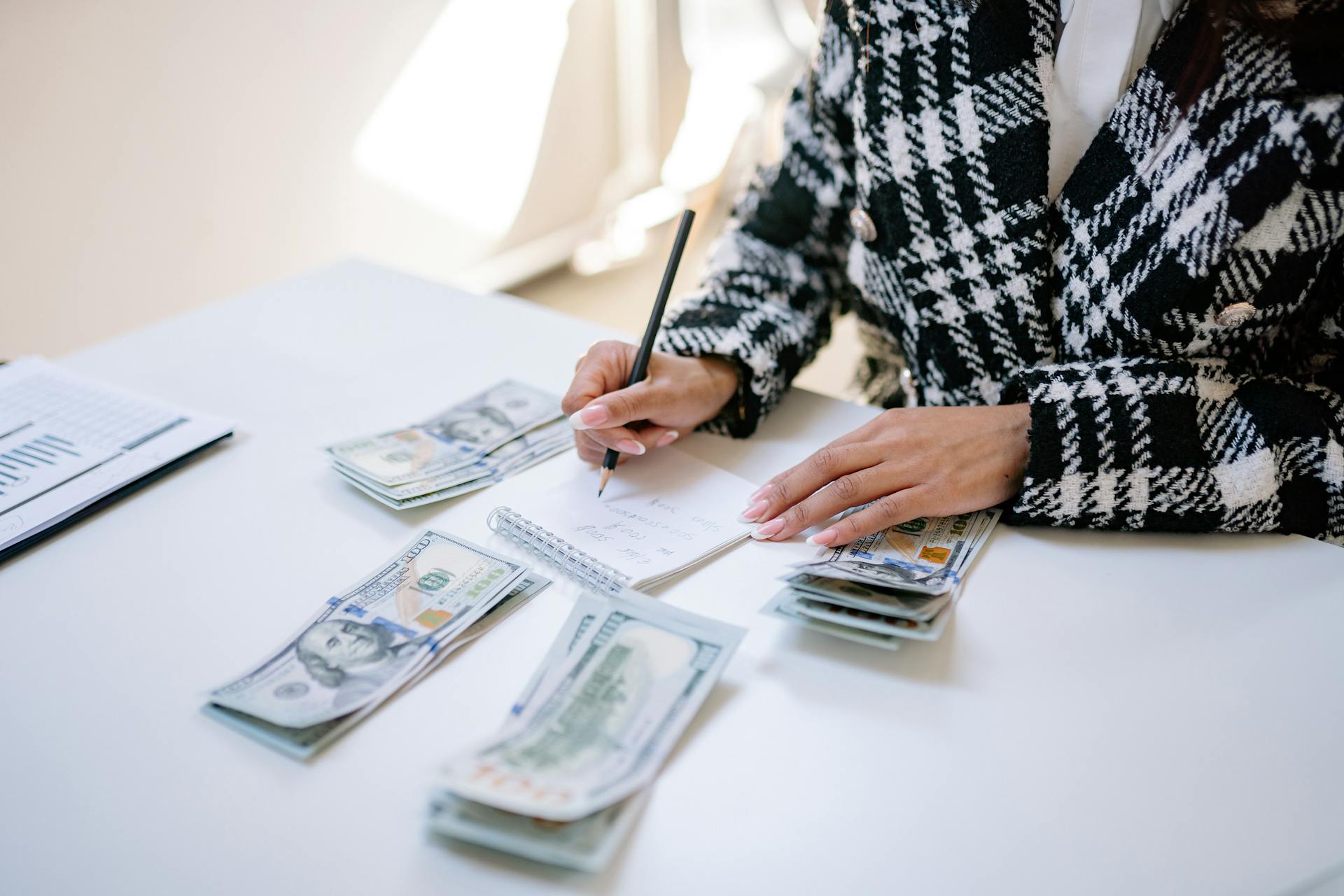 An adult woman counting cash and writing notes at a desk, showcasing financial planning