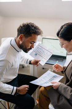 Two colleagues discussing data with charts and graphs in a modern office setting.