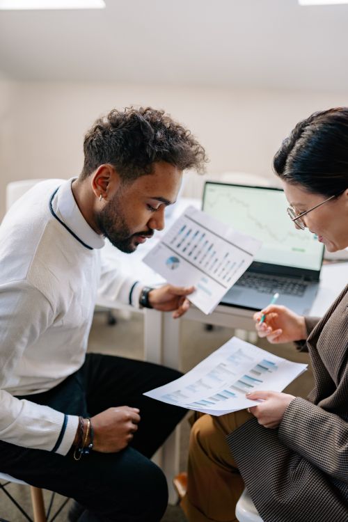 Free Two colleagues discussing data with charts and graphs in a modern office setting. Stock Photo