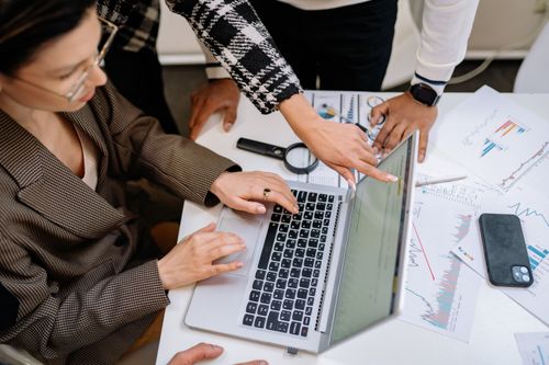 Free A group of colleagues working together on a laptop amidst documents. Collaborative teamwork in a modern office environment. Stock Photo