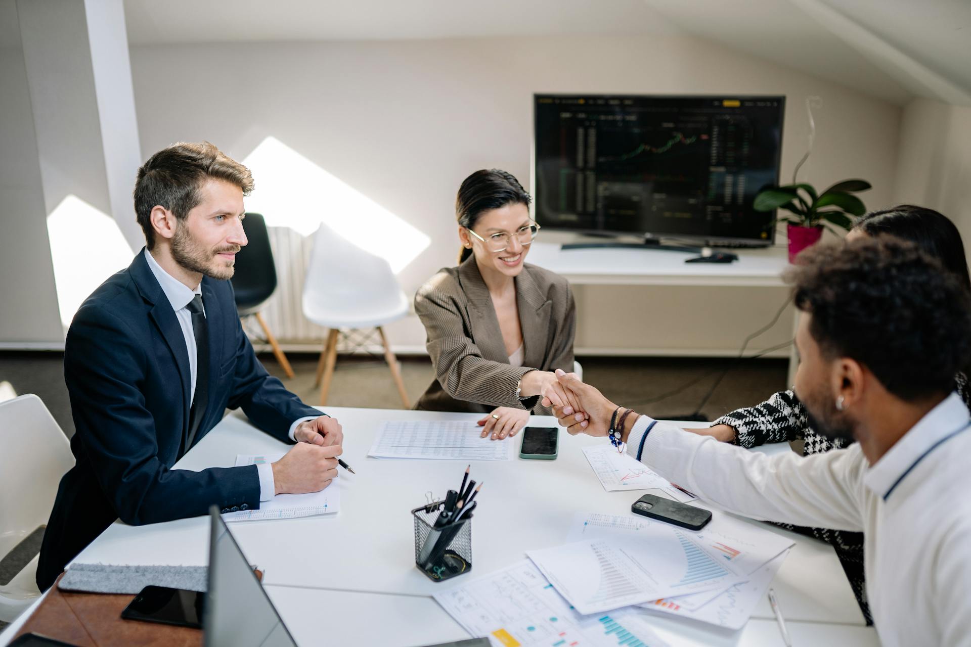 A diverse group of professionals in a business meeting shaking hands and discussing financial charts.