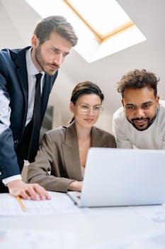 Three professionals collaborating around a laptop in a modern office setting.