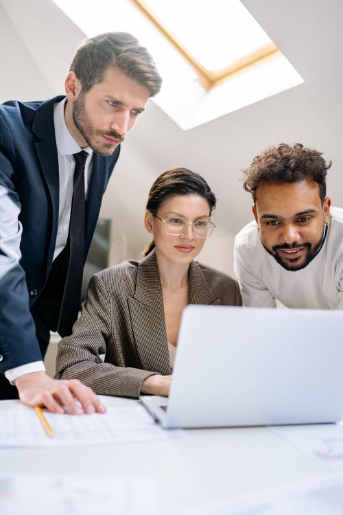 Free Three professionals collaborating around a laptop in a modern office setting. Stock Photo