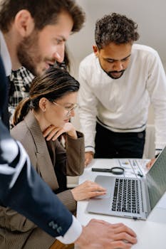 A diverse group of professionals collaborating on a laptop in an office setting.