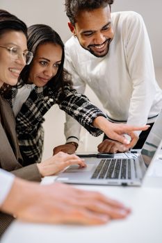 A diverse group of professionals working together focused on a shared laptop.