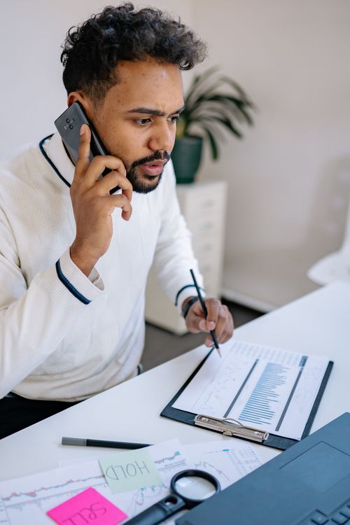 Free Young professional discussing finance reports over phone at modern workspace. Stock Photo