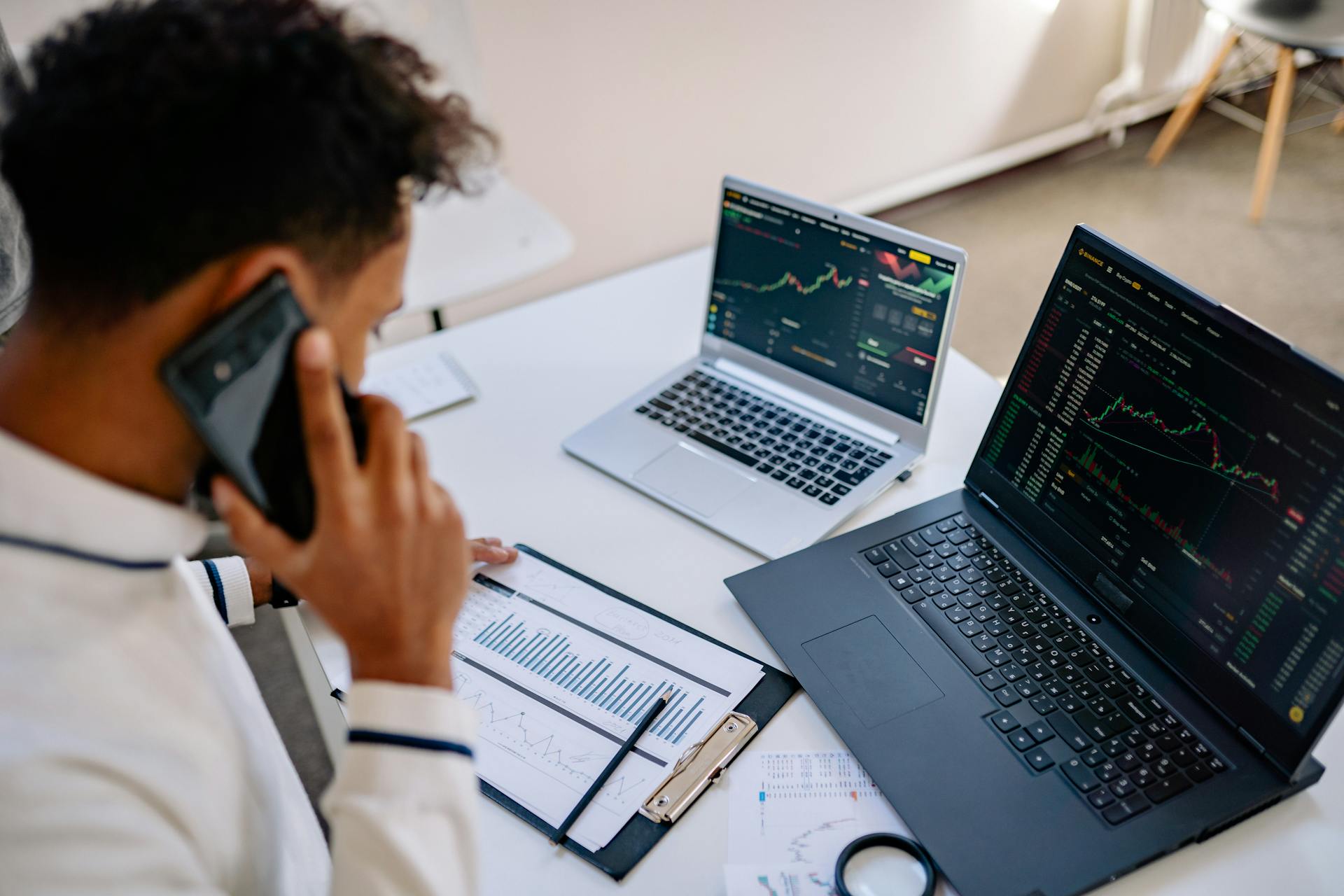 Man analyzing stock market charts on laptops while talking on a cellphone.