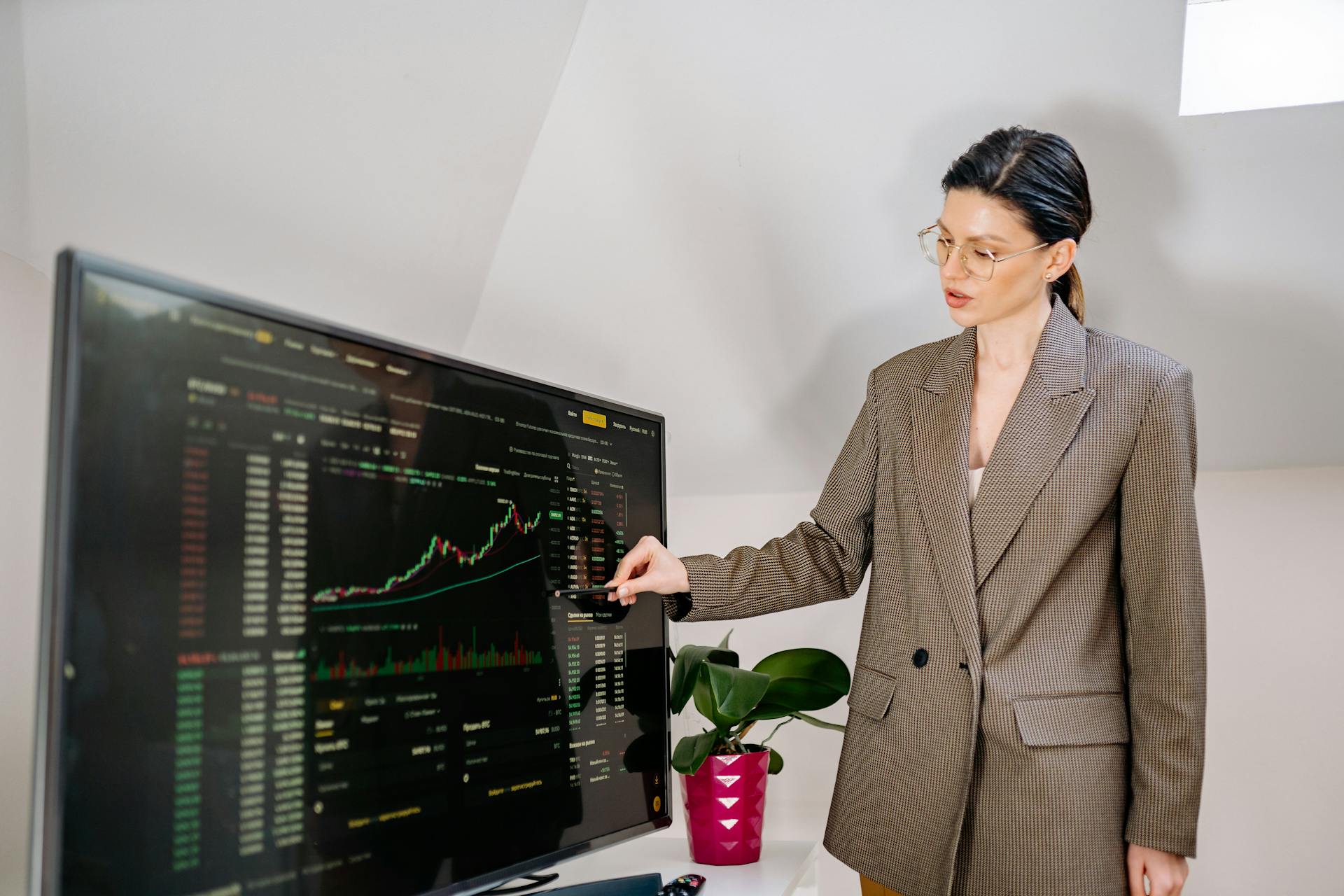 Businesswoman using stylus to highlight stock data on a monitor in office.