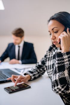 Focused businesswoman using smartphone while on call at modern office desk.