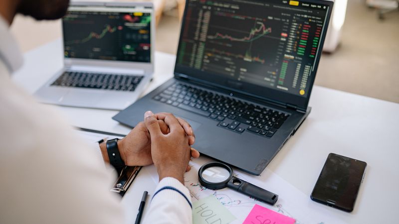 Business professional analyzing stock market data on dual laptops in an office.