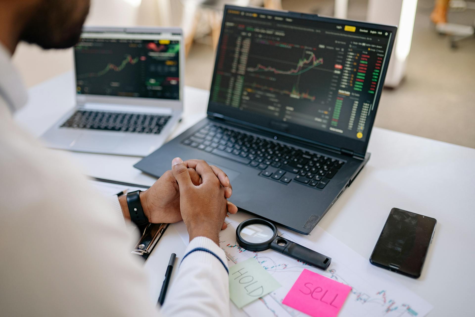 Business professional analyzing stock market data on dual laptops in an office.