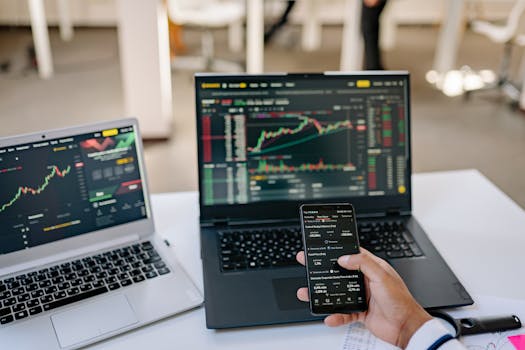 A professional tracks stock market trends using two laptops and a smartphone, showcasing digital finance tools.