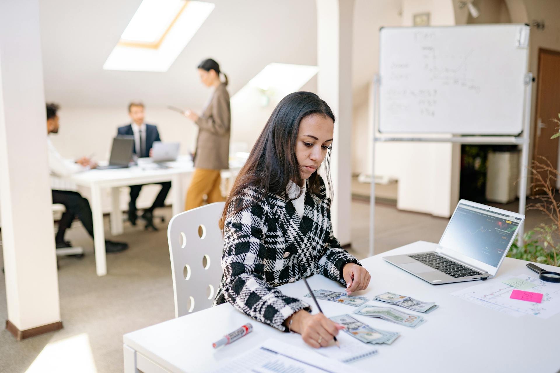 Focused businesswoman reviewing financial documents and currency in a modern office setting.