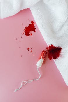 Tampon and bloody towel on pink background, symbolizing menstruation.