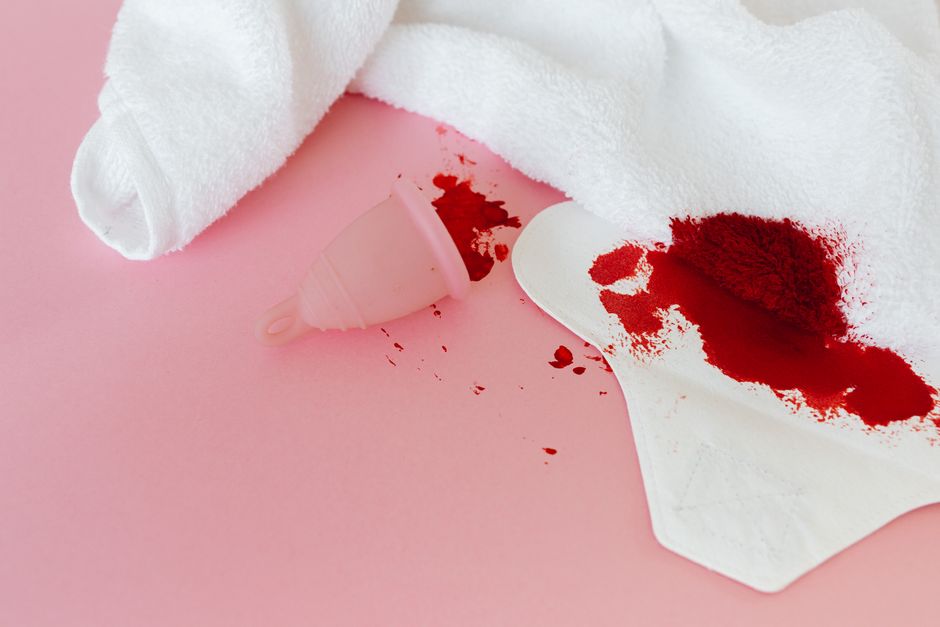 Menstrual cup and sanitary pad with blood stains on pink background, emphasizing menstrual hygiene.