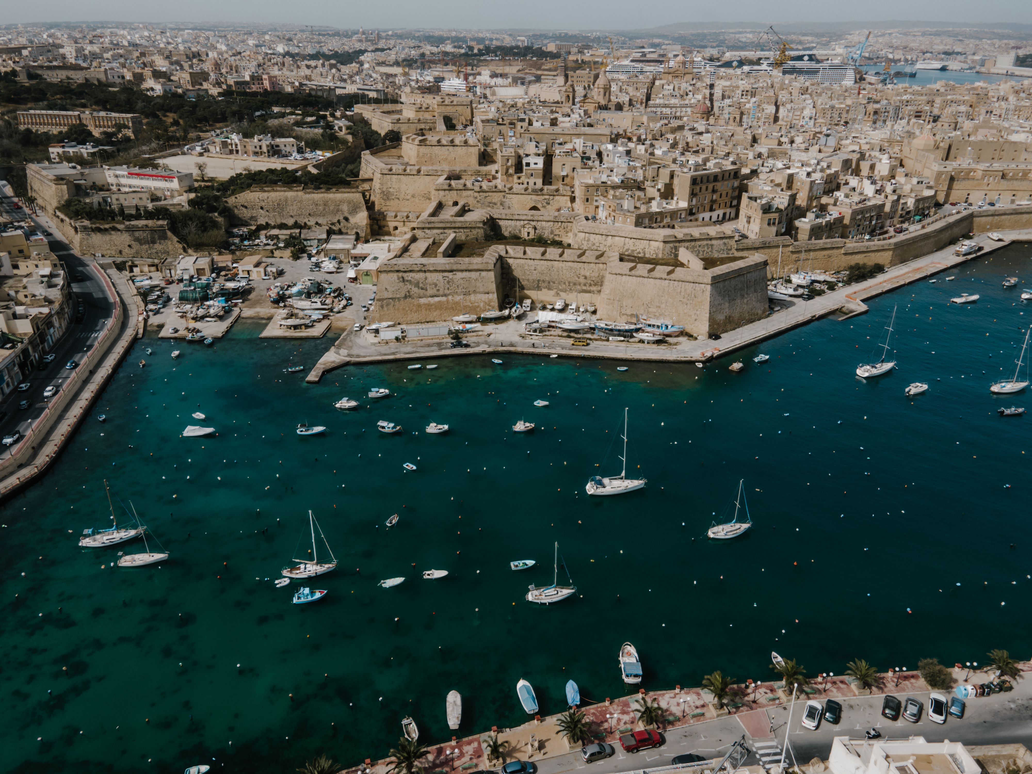 Aerial view of a coastal city with a historic fortress and boats anchored in clear blue harbor water