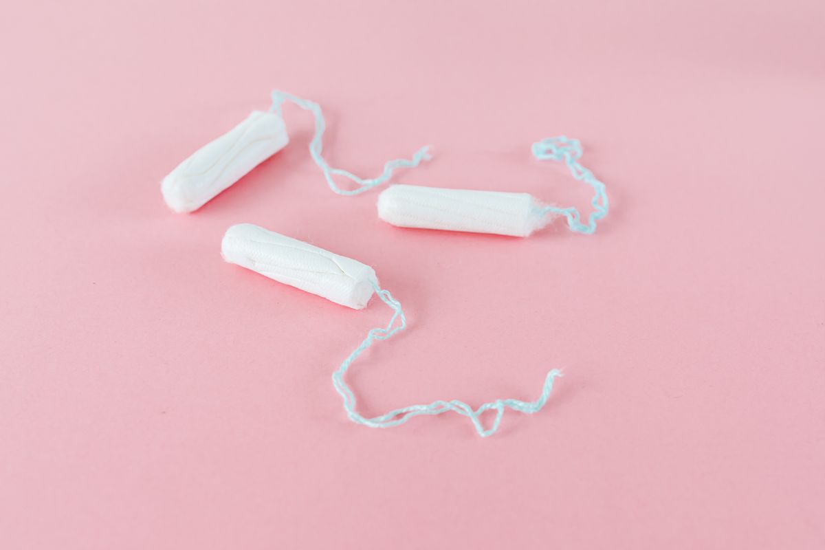 Three applicator-free cotton tampons with pale blue strings arranged on a soft pink background