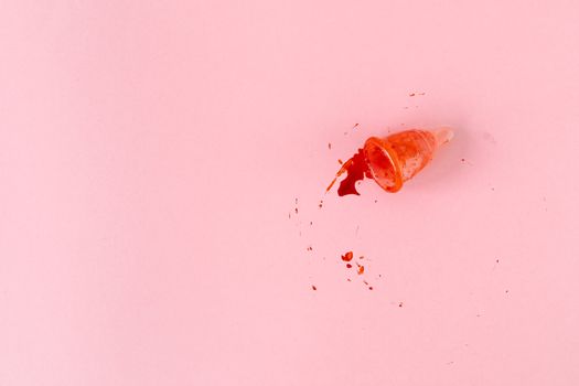A menstrual cup with spillage captured on a soft pink background, symbolizing menstruation.