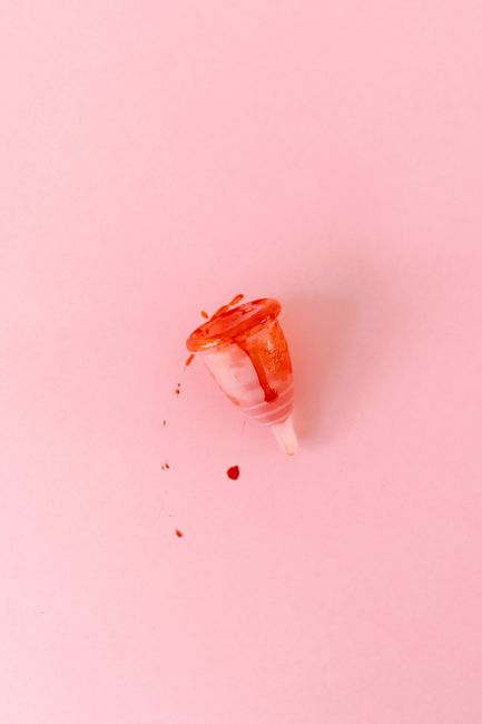 A menstrual cup with blood on a pastel pink background, symbolizing menstruation awareness.