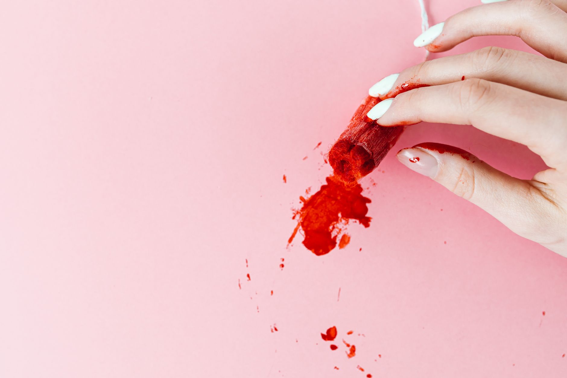 A close-up of a hand holding a tampon with blood on a pink background, symbolizing menstruation and menstrual health.