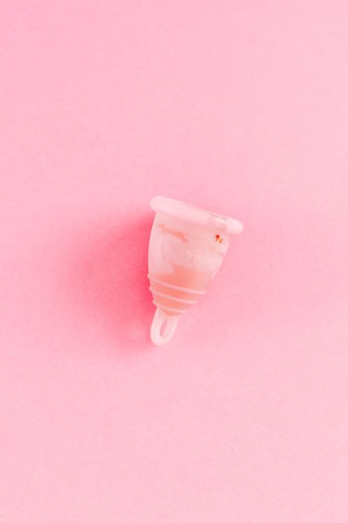 Free A menstrual cup with stains on a pink surface, symbolizing feminine hygiene. Stock Photo