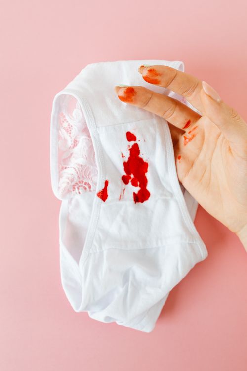 Free A hand holding white underwear with menstrual blood stains on a pink background, emphasizing menstrual health awareness. Stock Photo