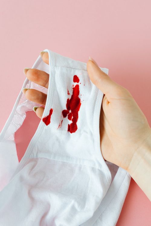 Free A person holding white underwear with menstrual blood stains on a pink background. Stock Photo