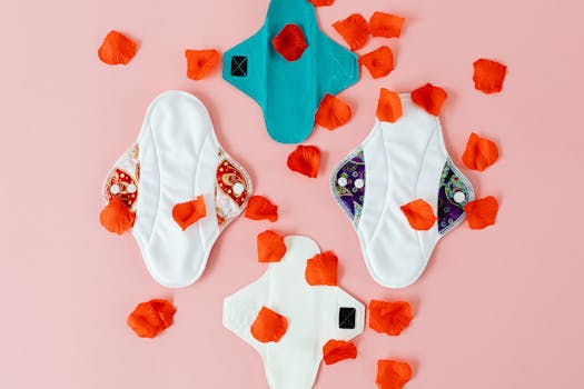 Colorful reusable menstrual pads with red petals on a pink background.