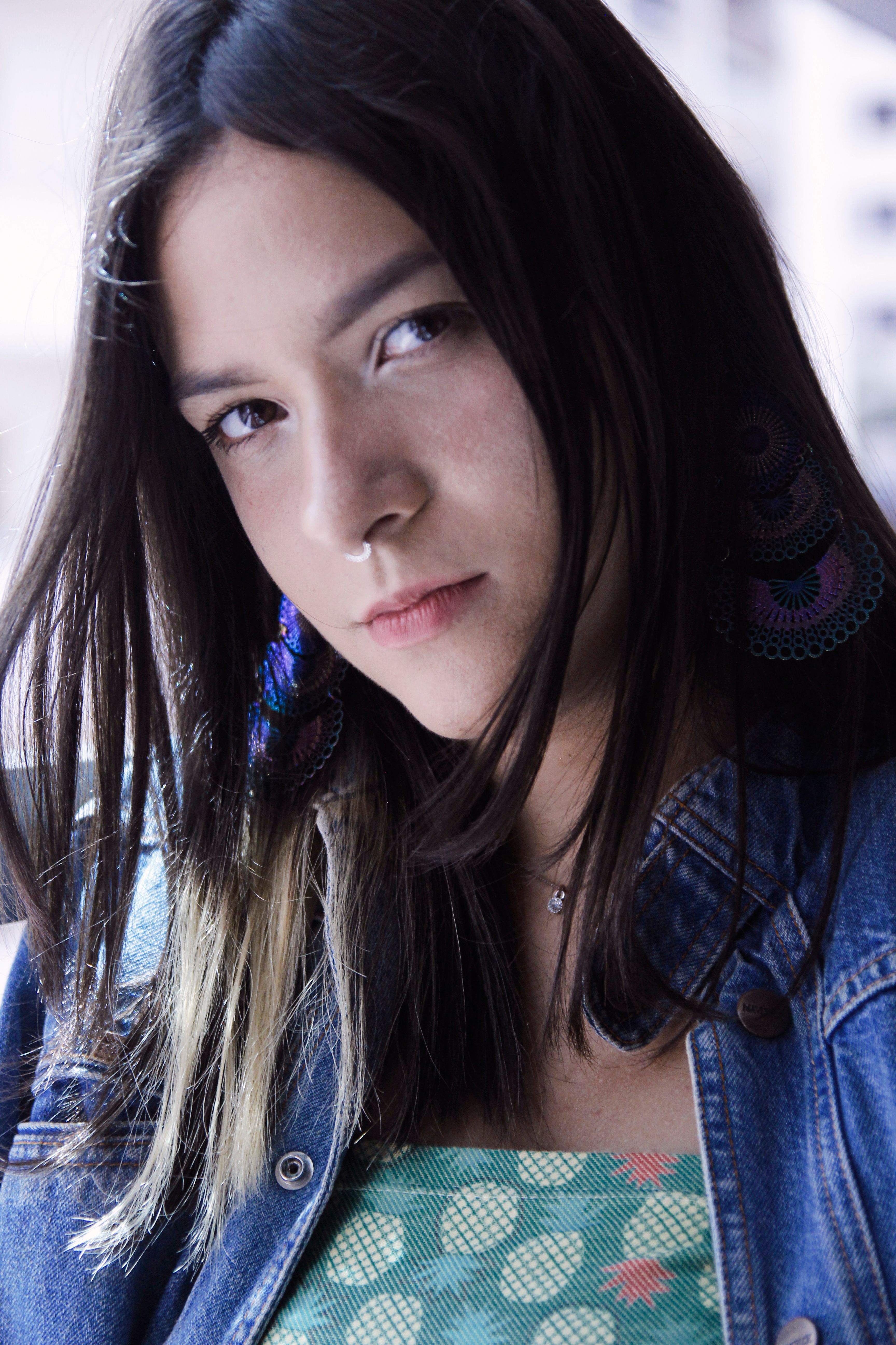 Close-up portrait of a woman with nose piercing in casual attire, outdoors.
