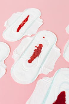 Menstrual pads with red blood stains on a pink background, top view.