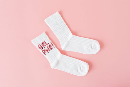 White socks on a pink background featuring empowering feminist slogan "Grl Pwr" in bright embroidery.