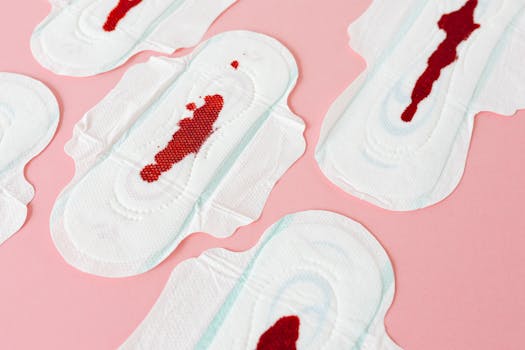 Close-up image of sanitary pads with blood stains on a pink background, representing menstruation.