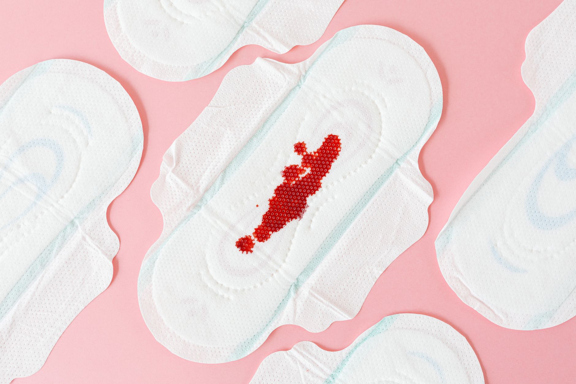 Flat lay of sanitary pads with red beads on pink surface, highlighting menstrual health.