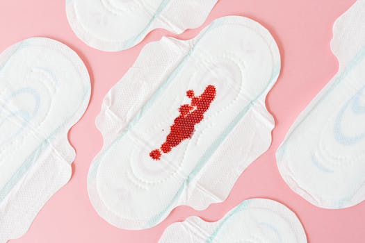 Flat lay of sanitary pads with red beads on pink surface, highlighting menstrual health.