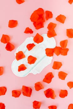 A sanitary pad surrounded by vibrant orange petals on a pink surface, symbolizing menstruation.