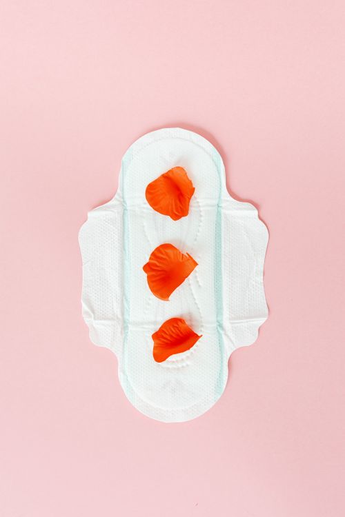 Free Artistic display of a sanitary pad with orange petals on a pink background, symbolizing menstruation. Stock Photo