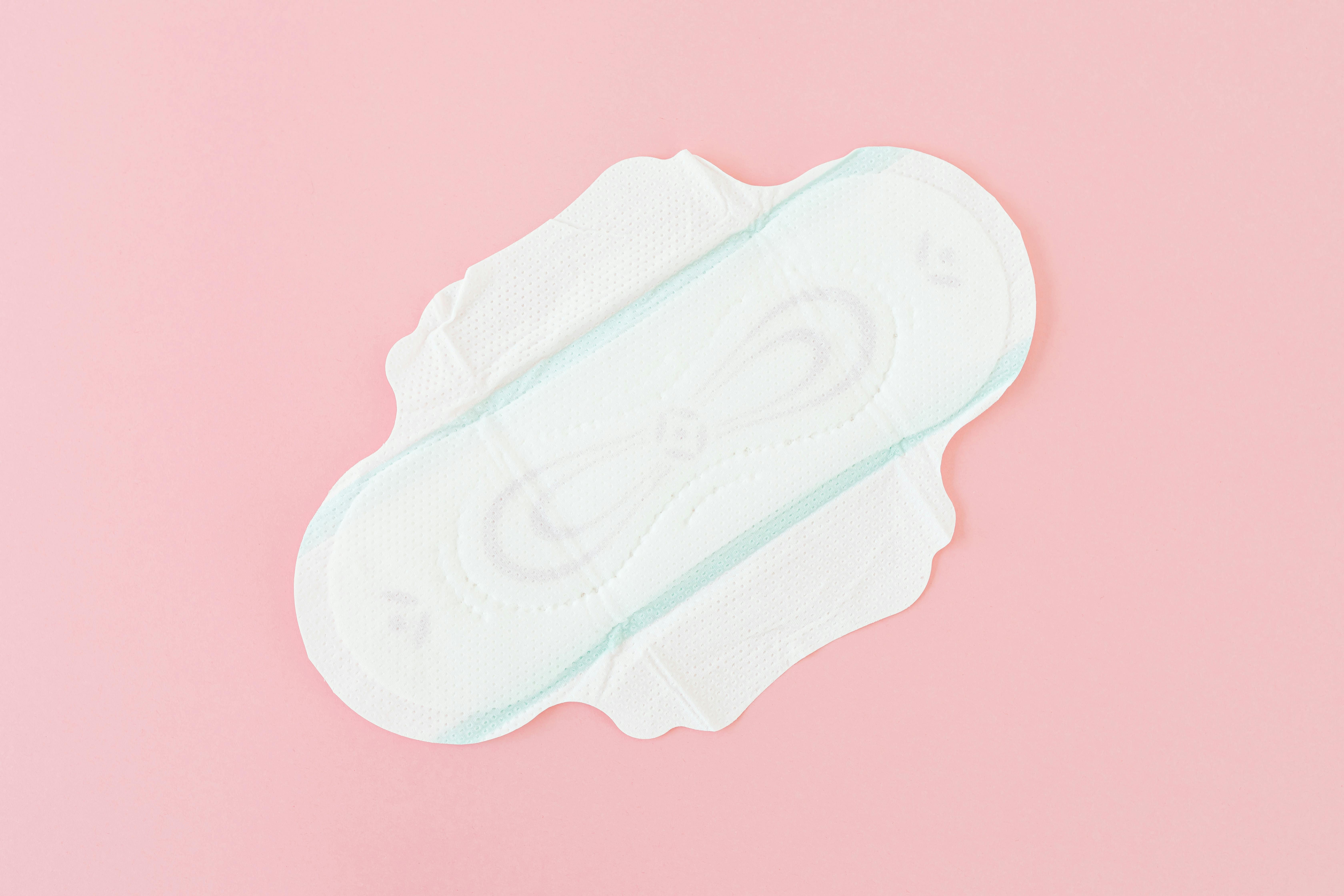 High-angle close-up of a sanitary pad on a pink background, emphasizing hygiene and care.