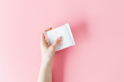 Free Close-up image of a hand holding a sanitary napkin on a pink background. Stock Photo