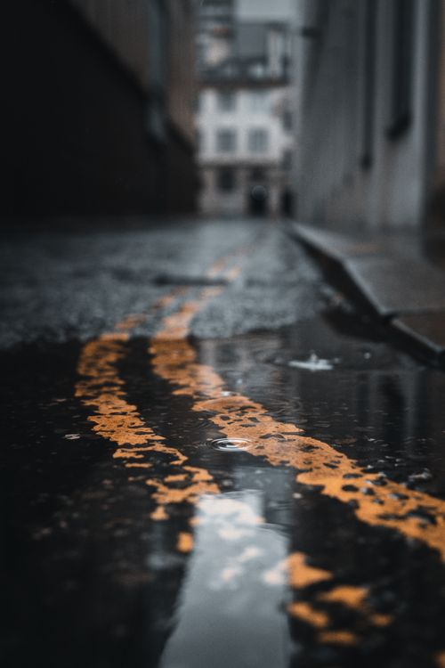 Free Captivating view of a wet urban street in Manchester featuring reflective puddles and a blurred background. Stock Photo
