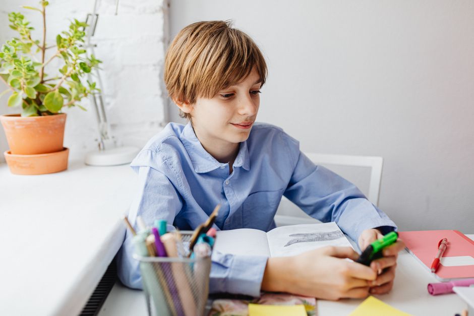 A boy in a blue shirt using a calculator at his desk, focused on learning and education.