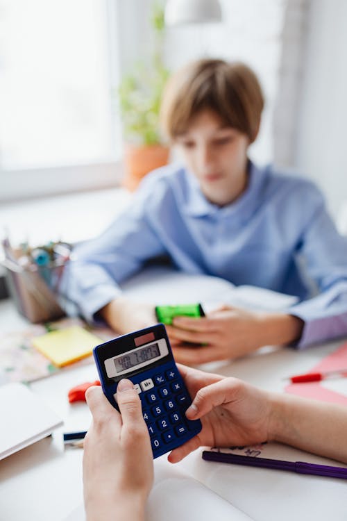 Person Sitting Beside a Boy in Blue Dress Shirt Using Calculators