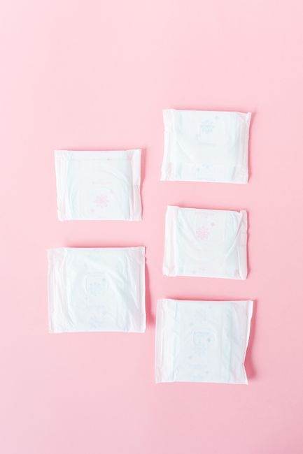 Flat lay of packaged sanitary pads on a soft pink background, emphasizing feminine hygiene.